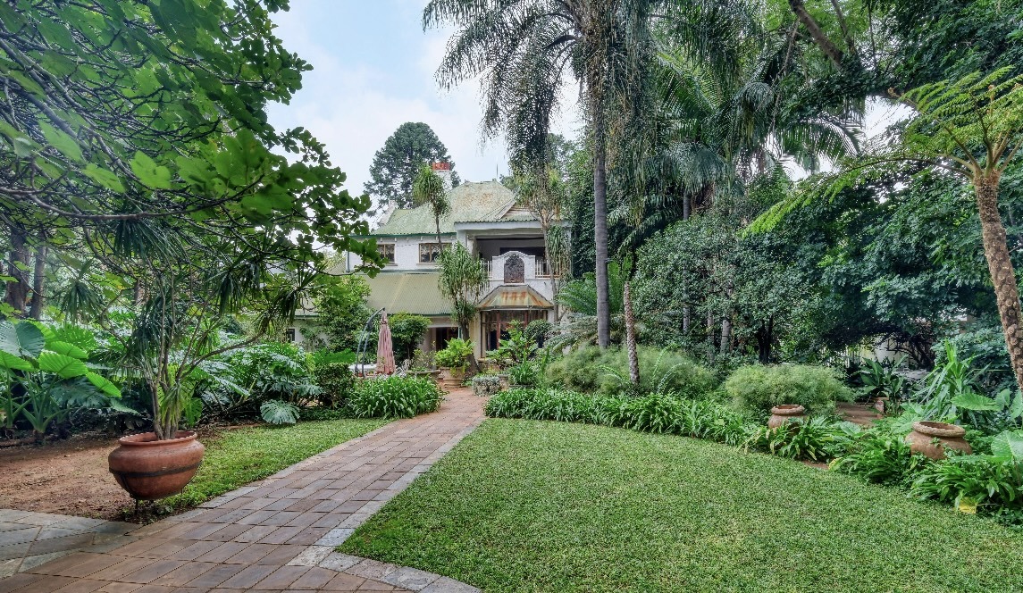 Established tropical garden with brick path, planted urns, and trimmed lawn