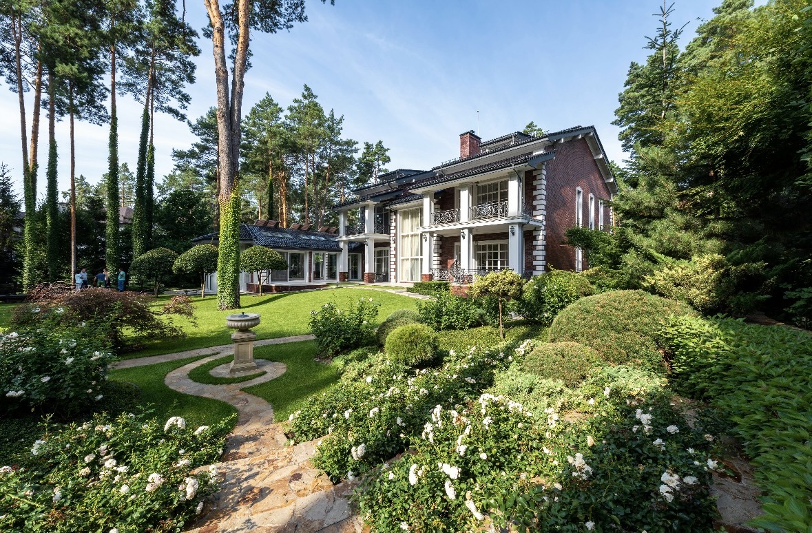 Formal garden with stone path, urn, and rose beds beside a brick home